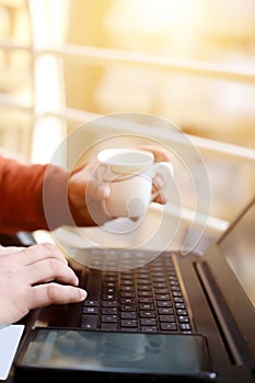 Man is using laptop with holding tea cup in hand
