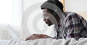 Man using laptop and listening music on headphones in bed