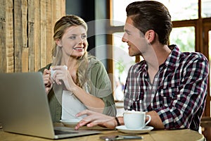 Man using laptop while looking at woman in coffee shop