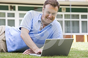 Man using laptop while lying in grass on campus