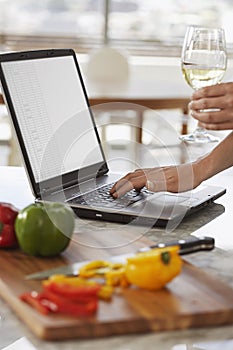 Man Using Laptop Next To Chopped Bellpepper In Kitchen photo