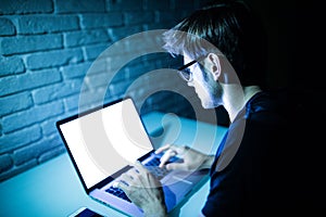Man using laptop in the night with white screen. Young hacker work on laptop in the night