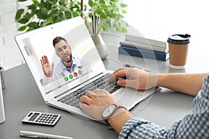 Man using laptop for online consultation with doctor via video chat at table photo