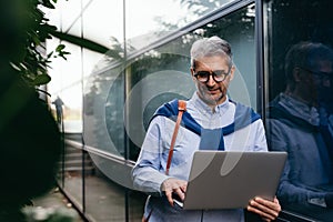 Man using laptop outdoor beside glass building