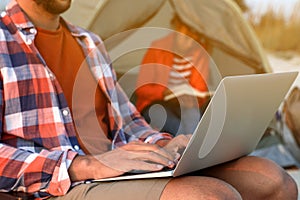 Man using laptop outdoors while his girlfriend reading book in camping tent, closeup