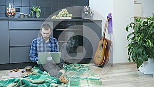 Man using laptop sitting on floor in living room. Male working from home. Man studying on notebook, typing on keyboard and searchi