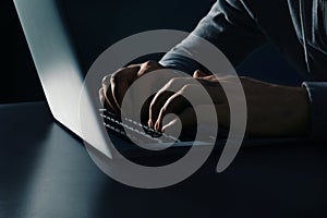 Man using laptop at table on dark background. Criminal activity