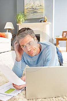 Man Using Laptop To Manage Bills Laying On Rug
