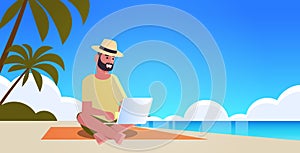 Man using laptop on tropical sea beach summer vacation online communication blogging concept seascape background full