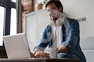 Man Using Laptop Wearing Headphones Relaxing Sitting On Sofa At Home.