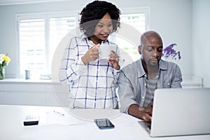 Man using laptop with woman holding coffee cup