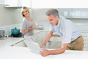 Man using laptop with woman in the kitchen