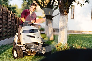 man using lawn tractor and cutting grass in garden during weekend time