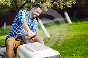 Man using lawn tractor for mowing grass in garden.