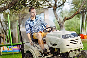 Man using lawn tractor for mowing grass in garden.