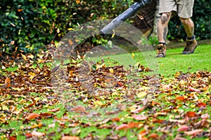 A man using a leaf blower machine to clear autumn leaves from a garden during fall