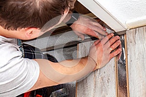 Man using measuring elbow and pencil while installing new wooden laminate flooring at home.