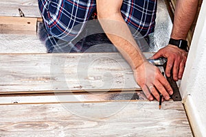 Man using measuring elbow and pencil while installing new wooden laminate flooring at home.