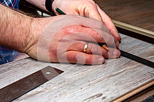 Man using measuring elbow and pencil while installing new wooden laminate flooring at home.