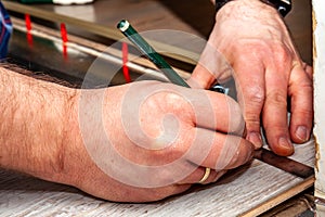 Man using measuring elbow and pencil while installing new wooden laminate flooring at home.