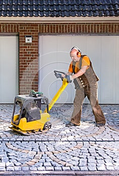 Man using a mechanical compacter on new pavers.