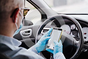 Man using mobile phone in a car wearing protective mask and gloves during pandemic coronacirus covid-19