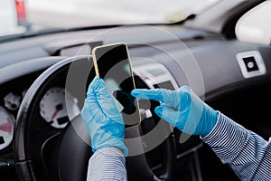 Man using mobile phone in a car wearing protective mask and gloves during pandemic coronacirus covid-19