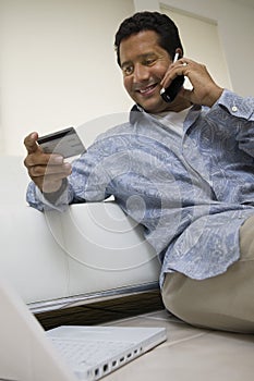 Man using mobile phone holding credit card in living room