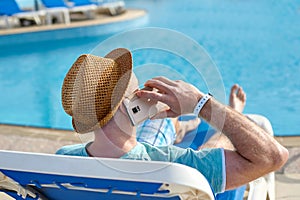 Man using mobile phone on vacation by the pool in hotel, concept of a freelancer working for himself on vacation and