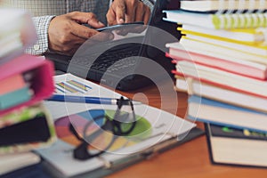 Man is using mobile phone and working with stack of documents on office desk