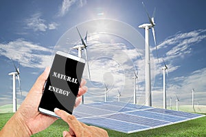 man using mobile smart phone control with Solar panels,wind turbines on green grass with blue sky background,natural Energy