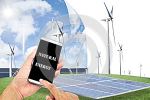 man using mobile smart phone control with Solar panels,wind turbines on green grass with blue sky background,natural Energy