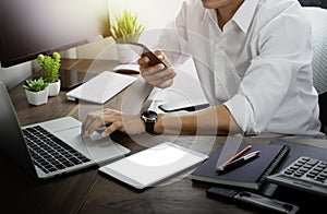 A man using mobile smartphone communicates on internet technology with typing keyboard of laptop computer on office desk.