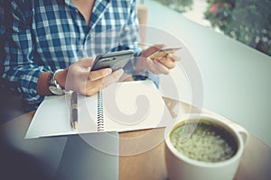 Man using mobile smartphone and credit card for online shopping in coffee shop, laptop computer notebook and coffee cup on table.
