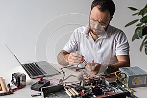 man using multimeter while fixing broken computer and looking down