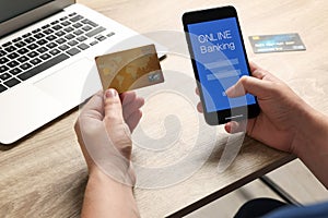 Man using online banking app on smartphone and credit card at wooden office table, closeup