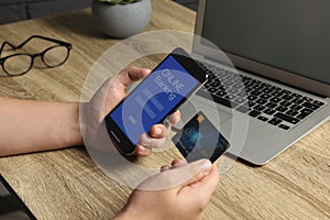 Man using online banking app on smartphone and credit card at wooden office table, closeup