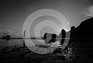 Man using a phone to take pictures of the morning sunrise on the beach, reflection on the water