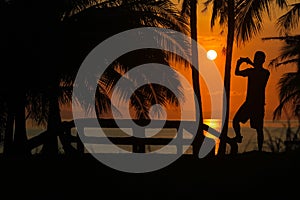 Man using a phone to take pictures of the morning sunrise on a coconut beach