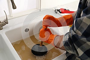 Man using plunger to unclog sink drain in kitchen