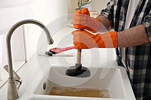 Man using plunger to unclog sink drain in kitchen