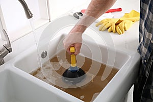 Man using plunger to unclog sink drain in kitchen, closeup