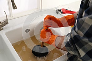 Man using plunger to unclog sink drain in kitchen photo