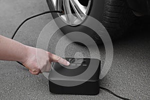 Man using portable air pump to inflate car tire outdoors, closeup