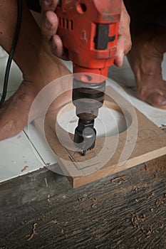 A man using powered drill with a hole saw bit to make precision hole in a wooden plank.