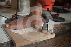 A man using powered drill with a hole saw bit to make precision hole in a wooden plank.