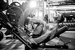 Man Using A Press Machine In A Fitness Club. Strong man doing an exercise on its feet in the simulator.