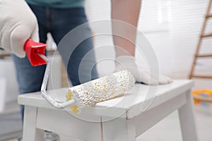 Man using roller to paint bekvam with white dye indoors, closeup