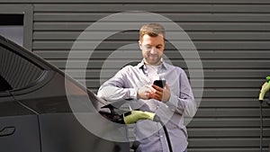 A man using smart phone and charging car at vehicle charging station