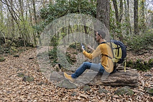 Man using smart phone sitting with backpack on a tree in forest.Travel concept, walk, excursionist, hiker outdoor lifestyle.Copy